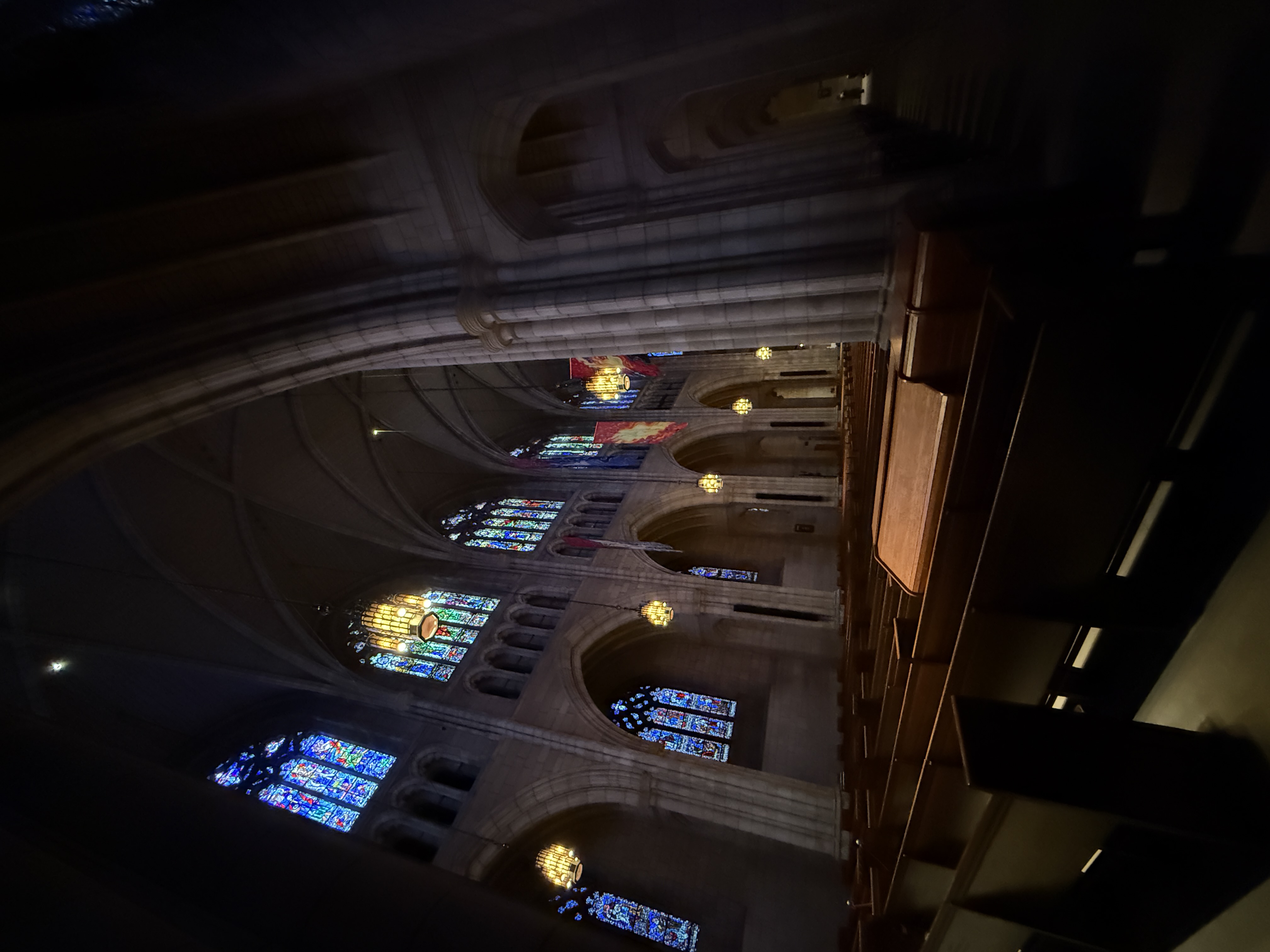 Dim view down the chapel nave with repeated pointed arches and glowing stained-glass windows