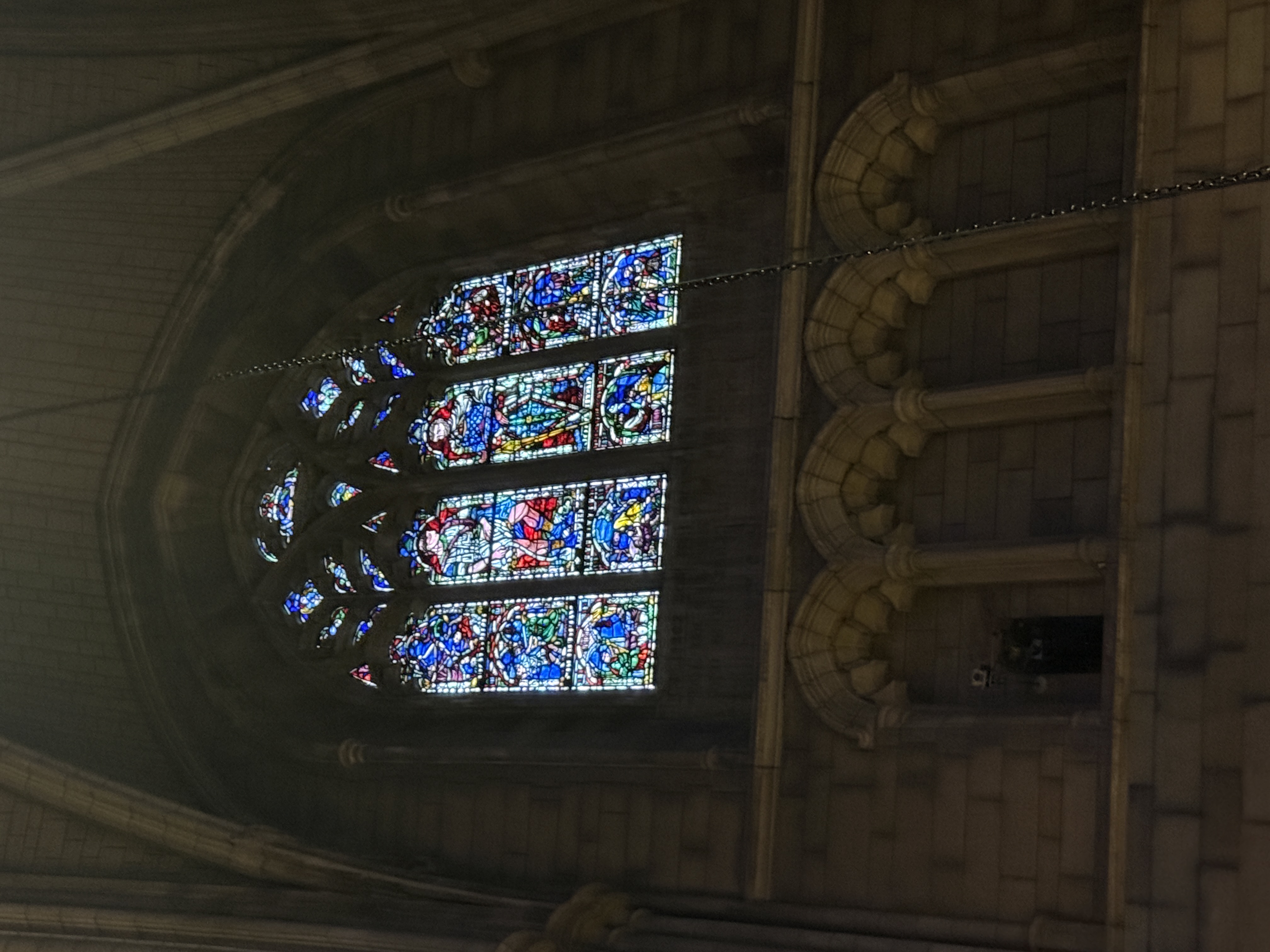 Stained-glass window framed by a broad stone arch and upper gallery openings