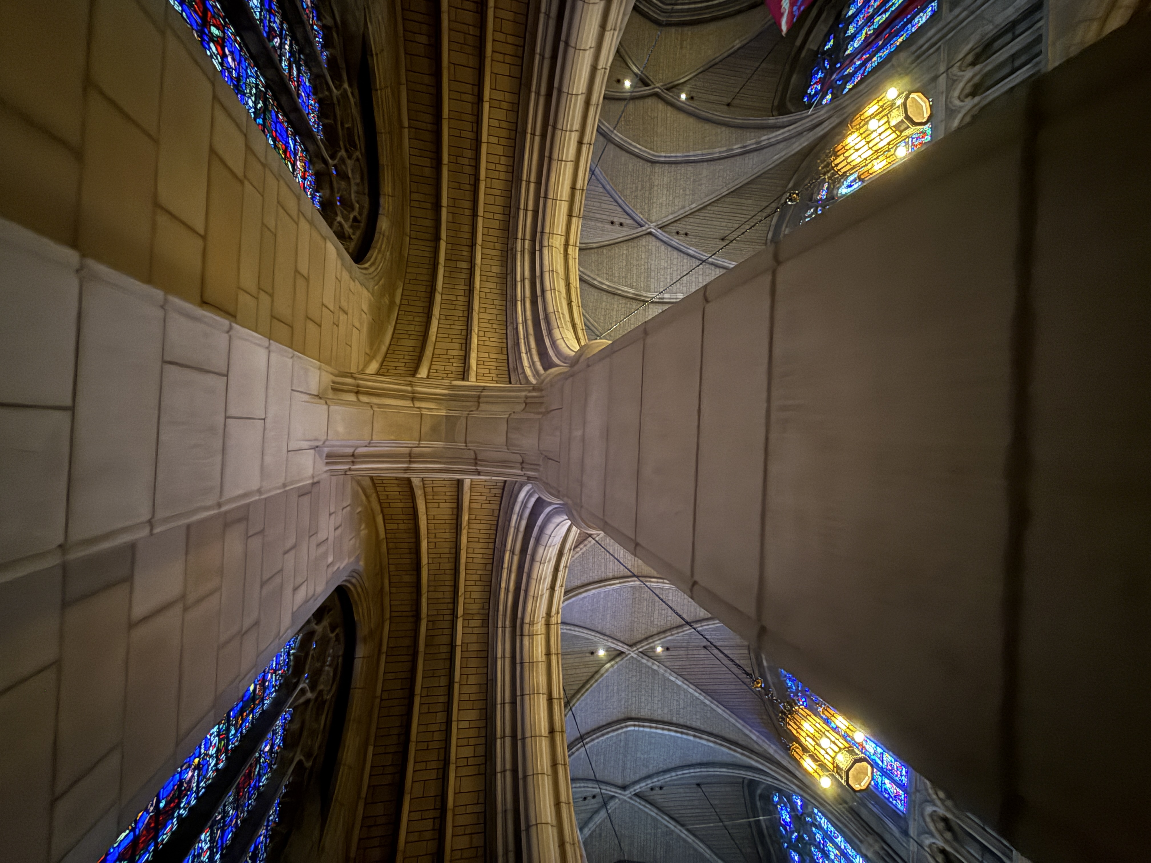 Upward view of intersecting stone arches and vault ribs between stained-glass windows