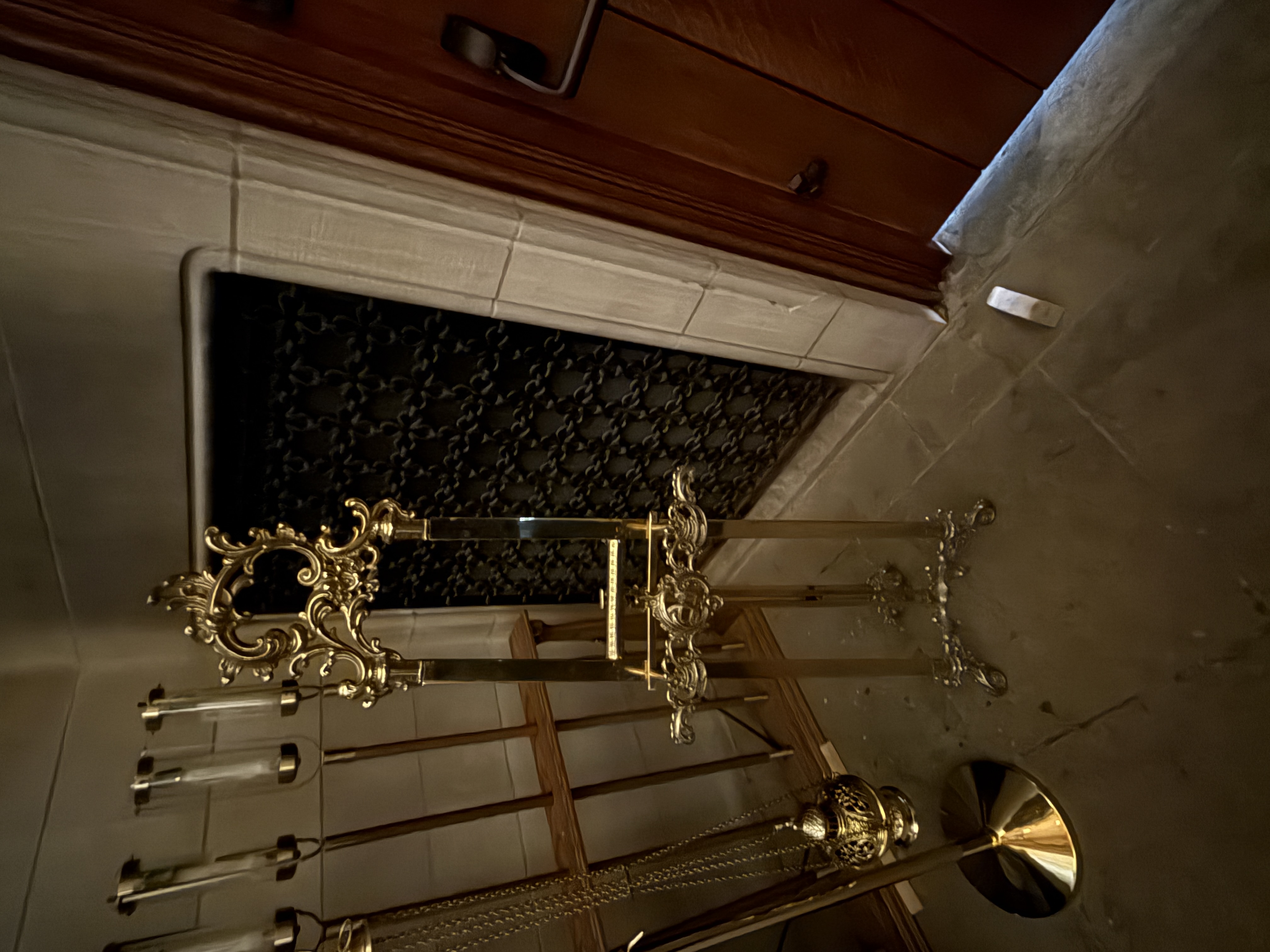 Brass processional stand and hanging censer arranged beside a dark floor grille