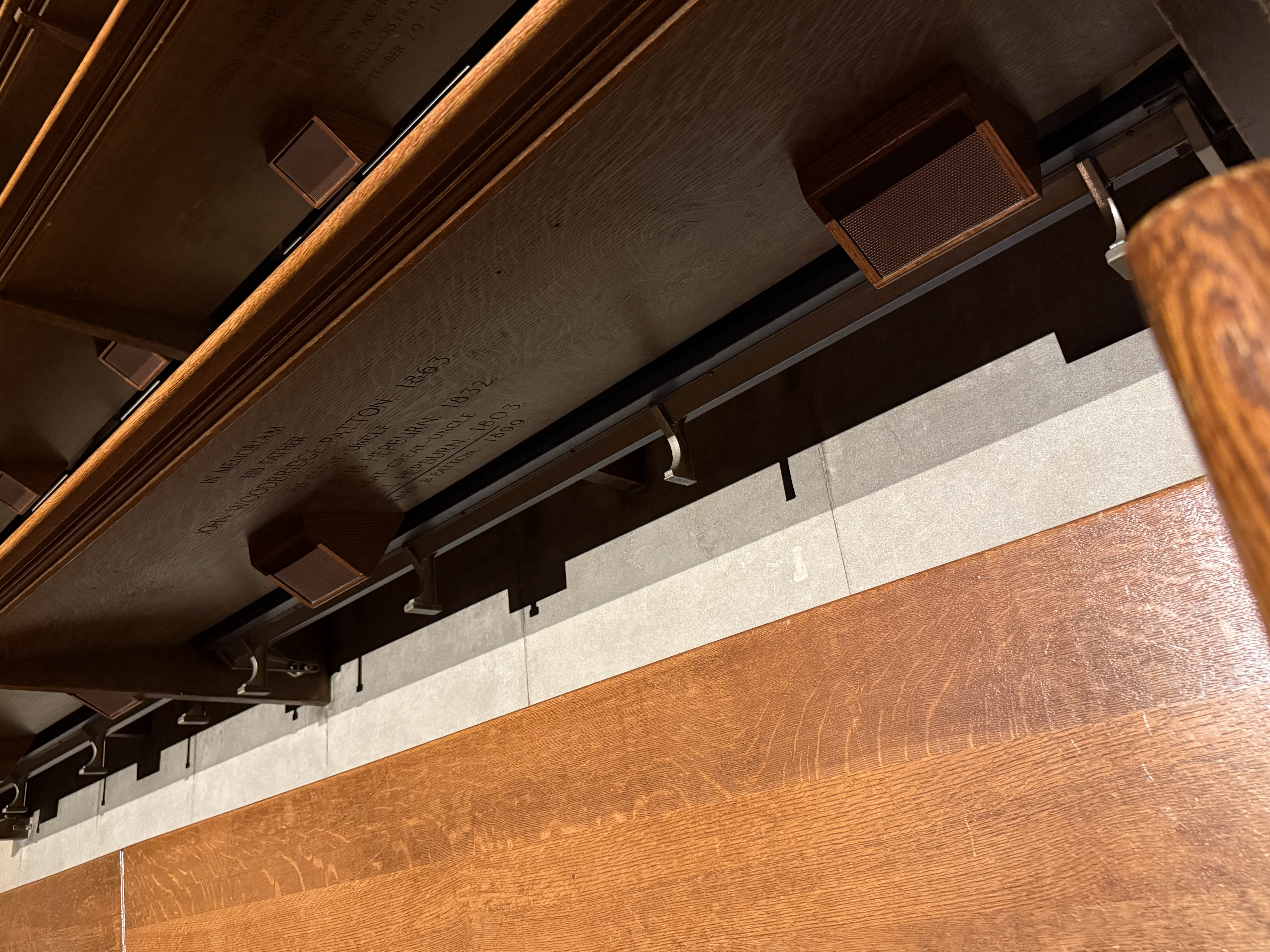 Underside of dark wooden choir seating with carved inscriptions and supports