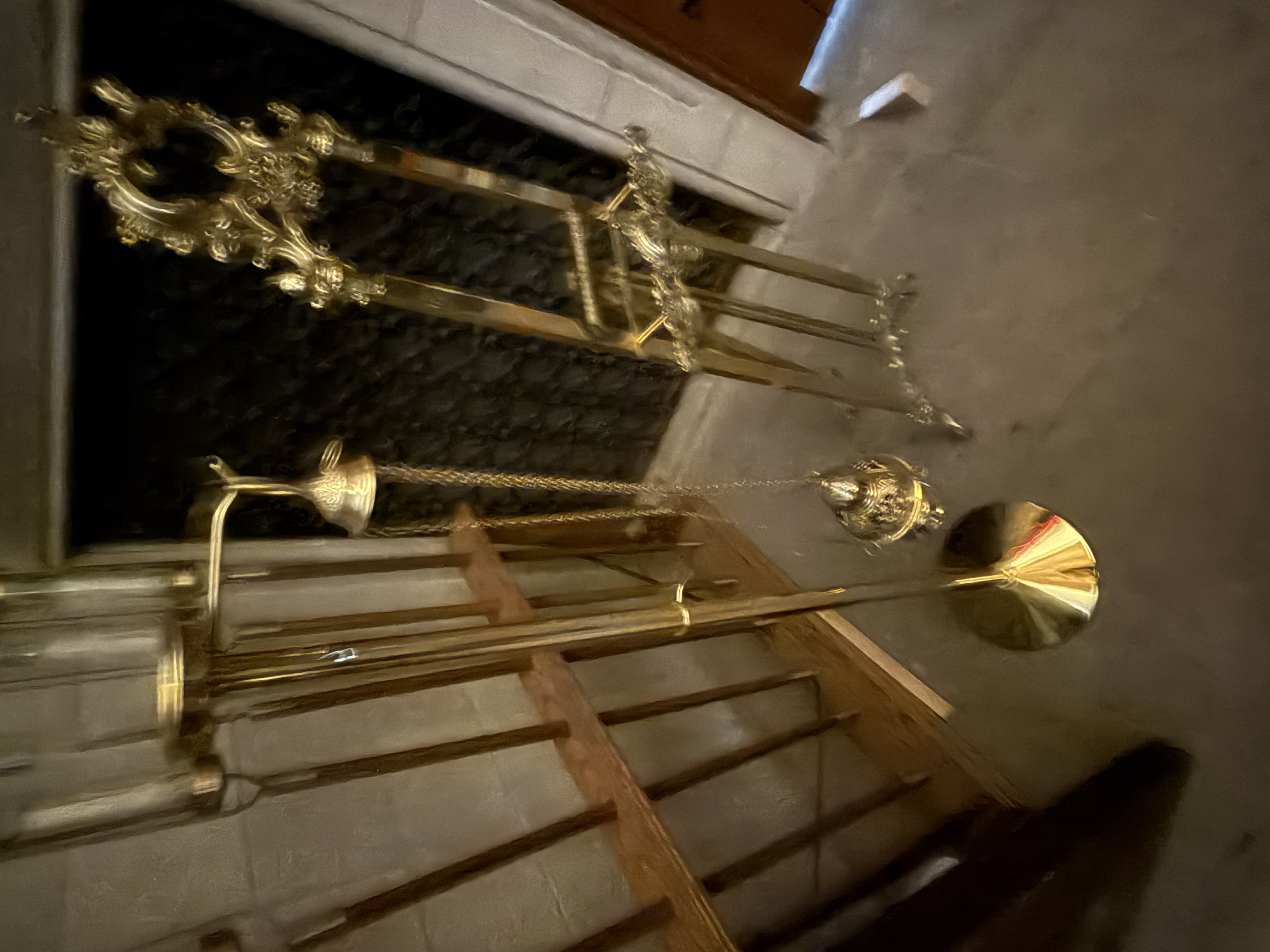 Rack holding long brass candle lighters and snuffers beside a floor grille