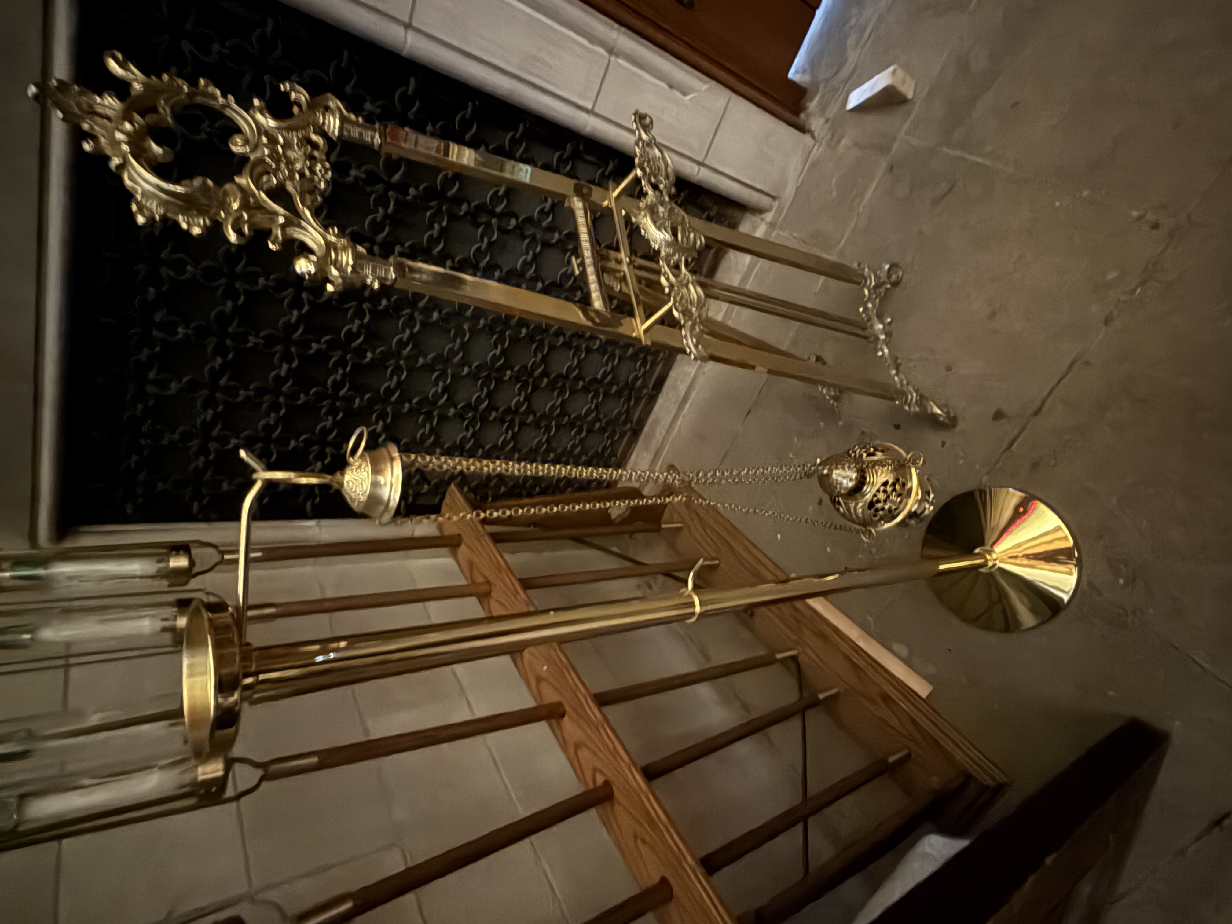 Blurred view of brass church implements including a hanging censer and ornate stand