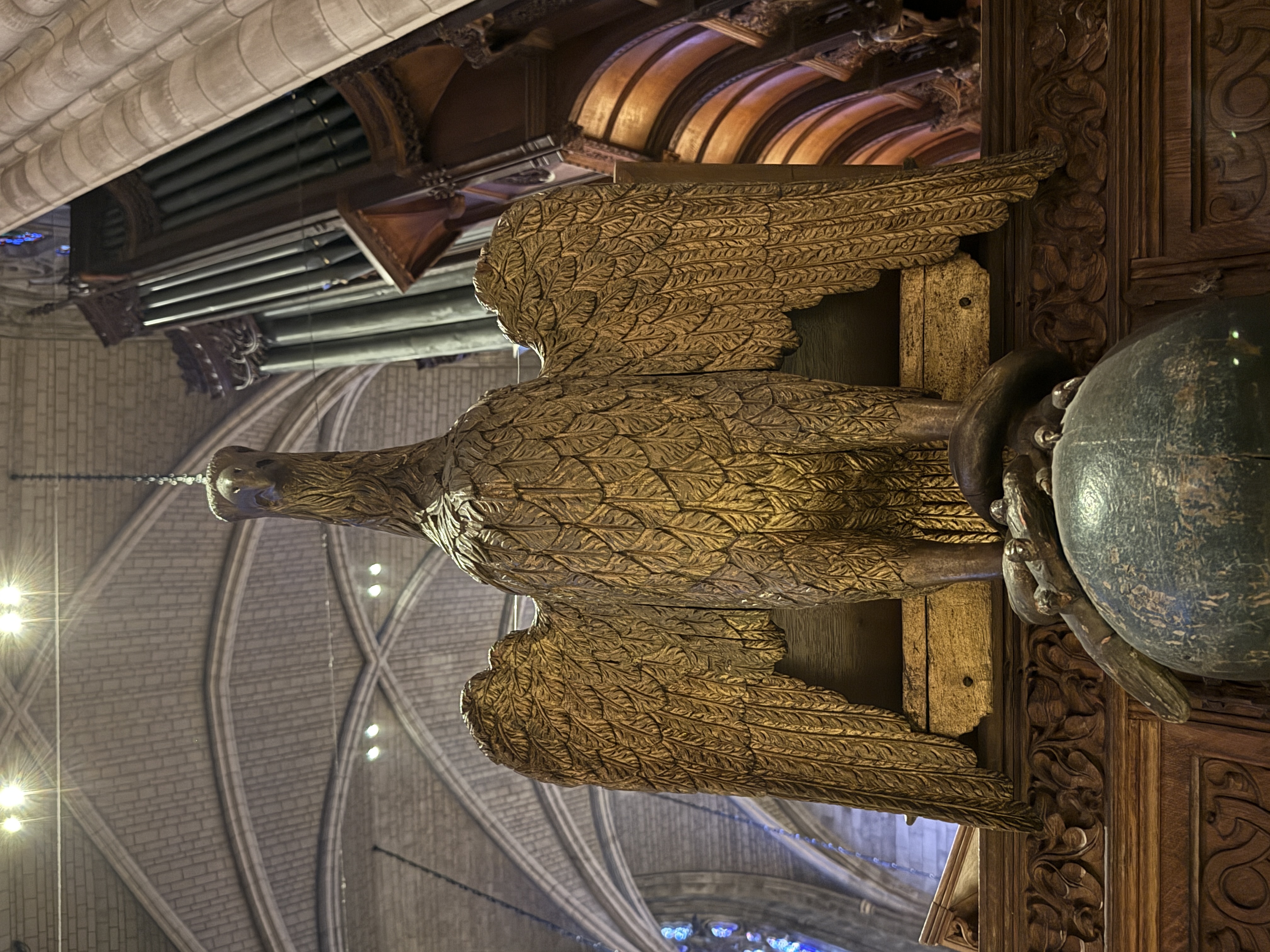 Carved eagle figure perched above dark woodwork with organ pipes behind it