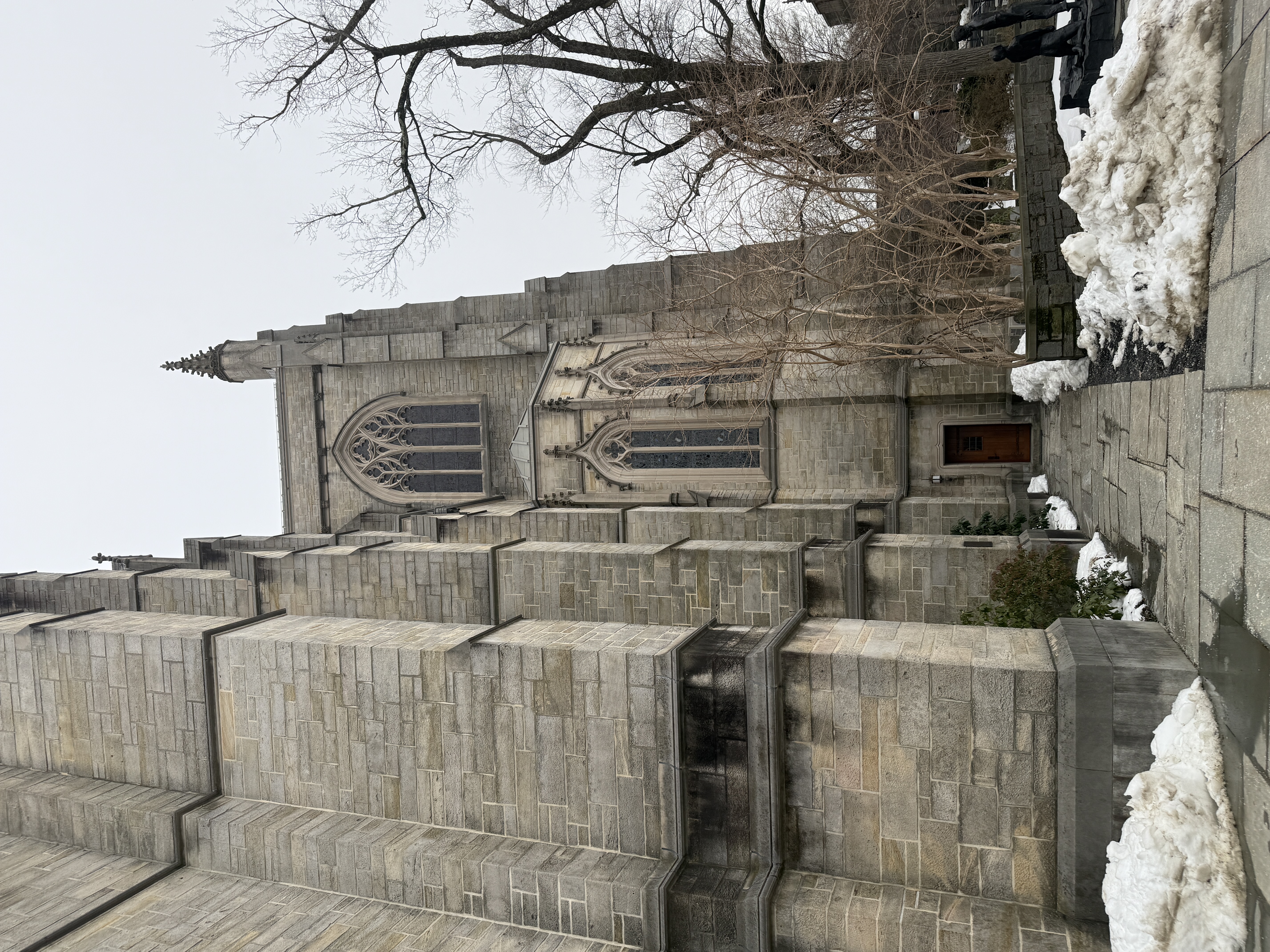 Buttressed stone chapel exterior with tall windows and snow along the walkway