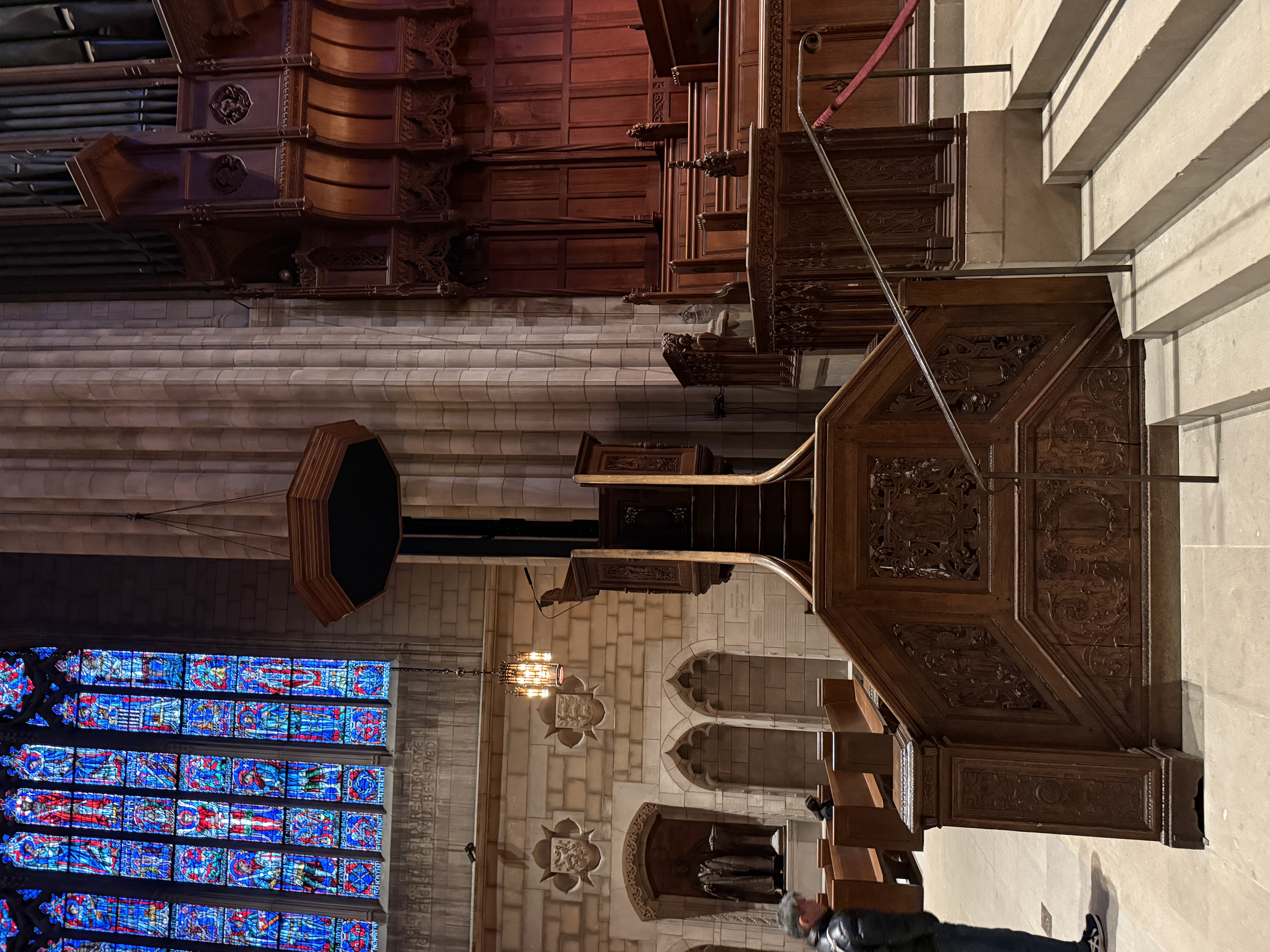 Chapel interior with carved wooden pulpit, stained-glass window, and decorative shields on the wall