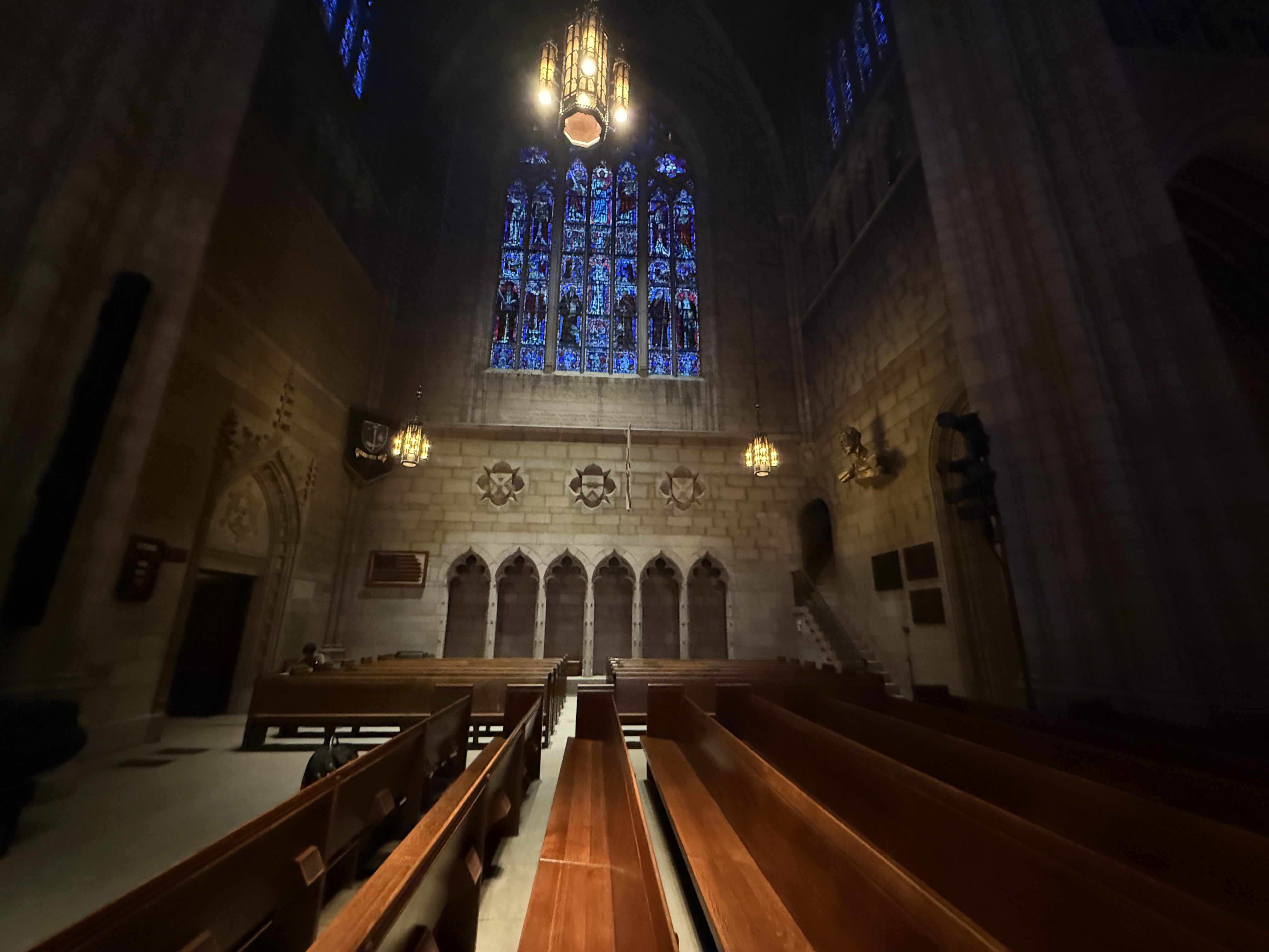 Wide view of the chapel nave with pews, chandeliers, stained glass, and shield carvings above the arches