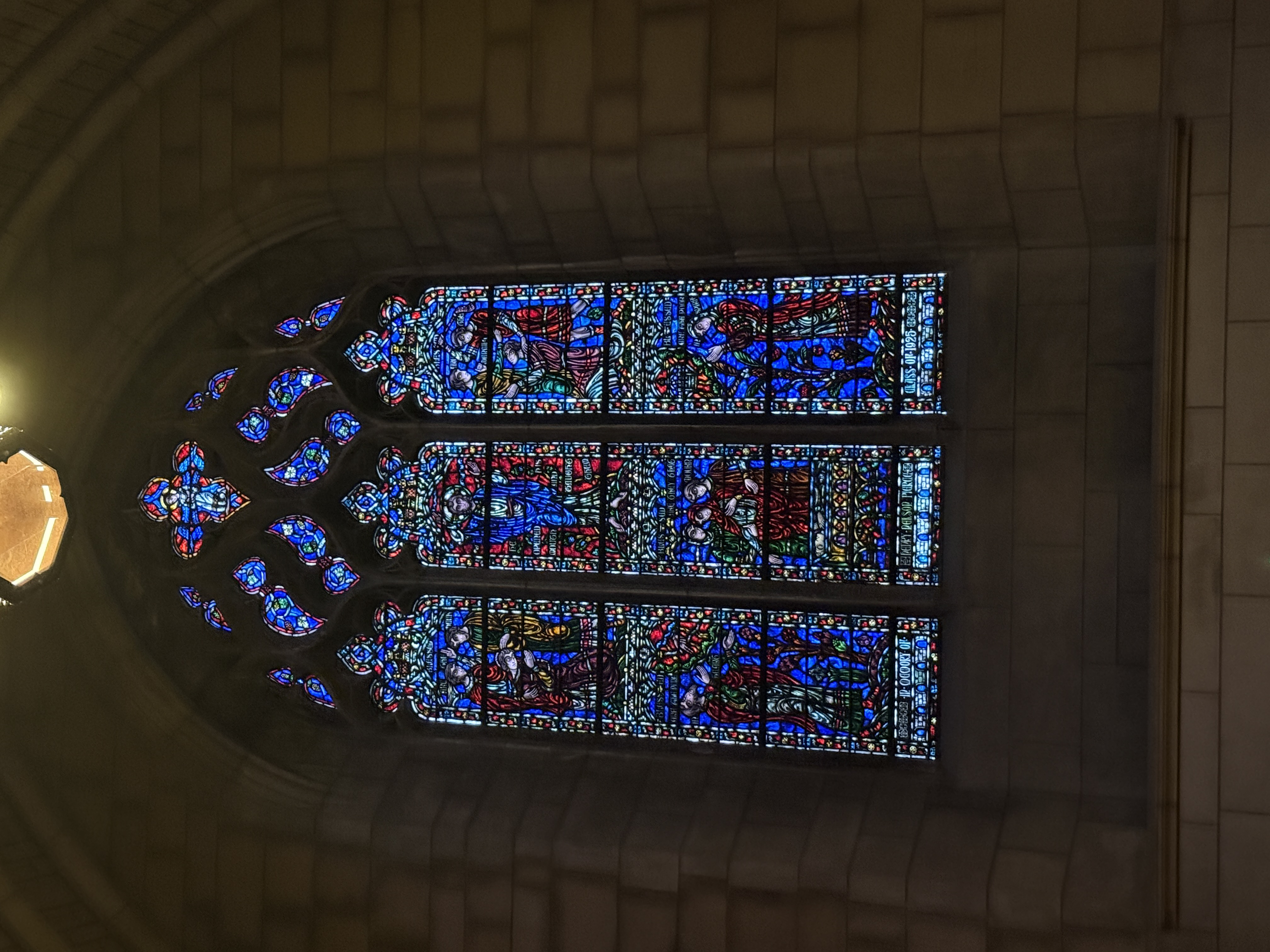 Three-panel stained-glass window filled with red and blue biblical scenes