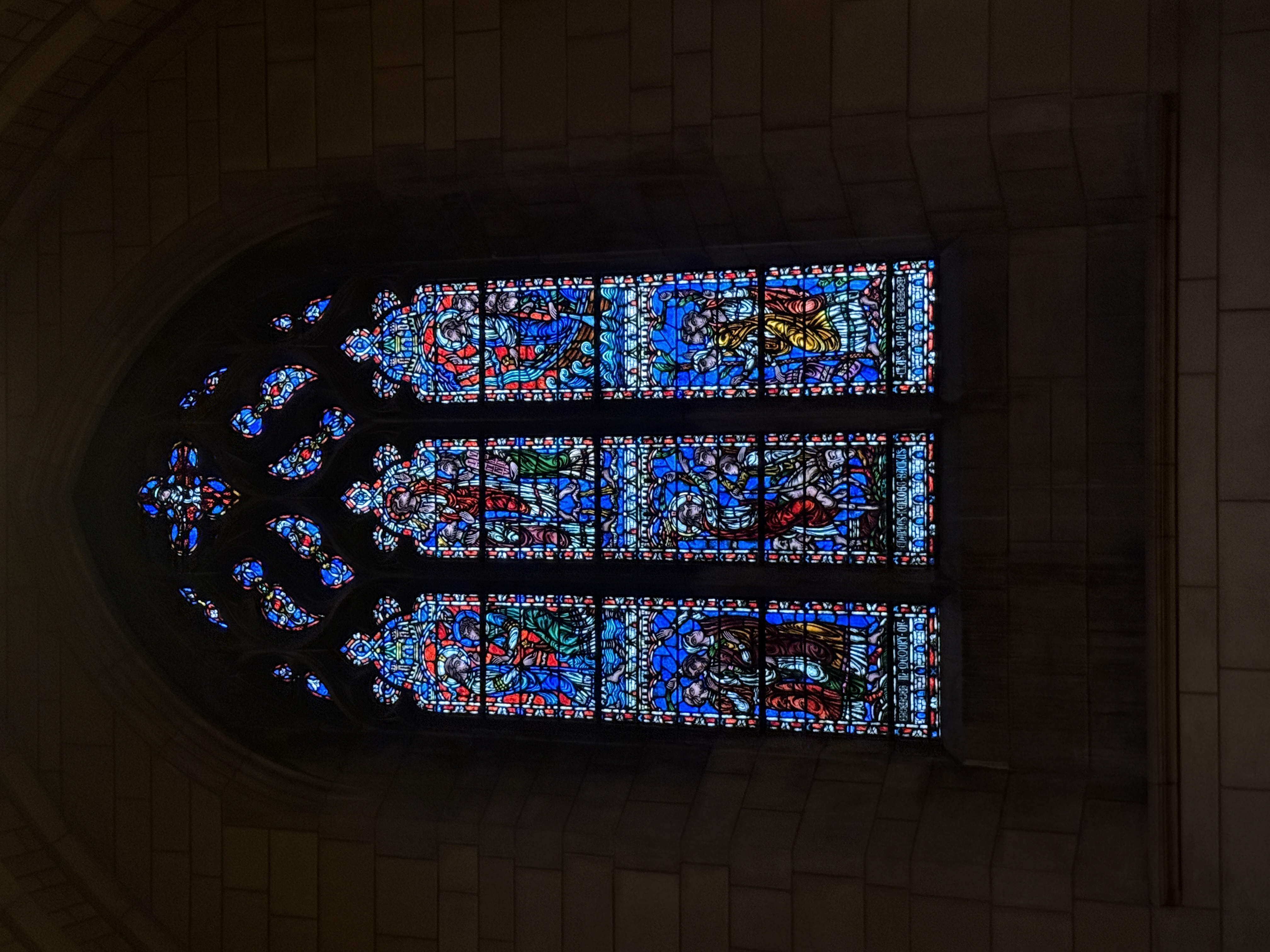 Tall stained-glass lancet window with robed figures and circular tracery lights