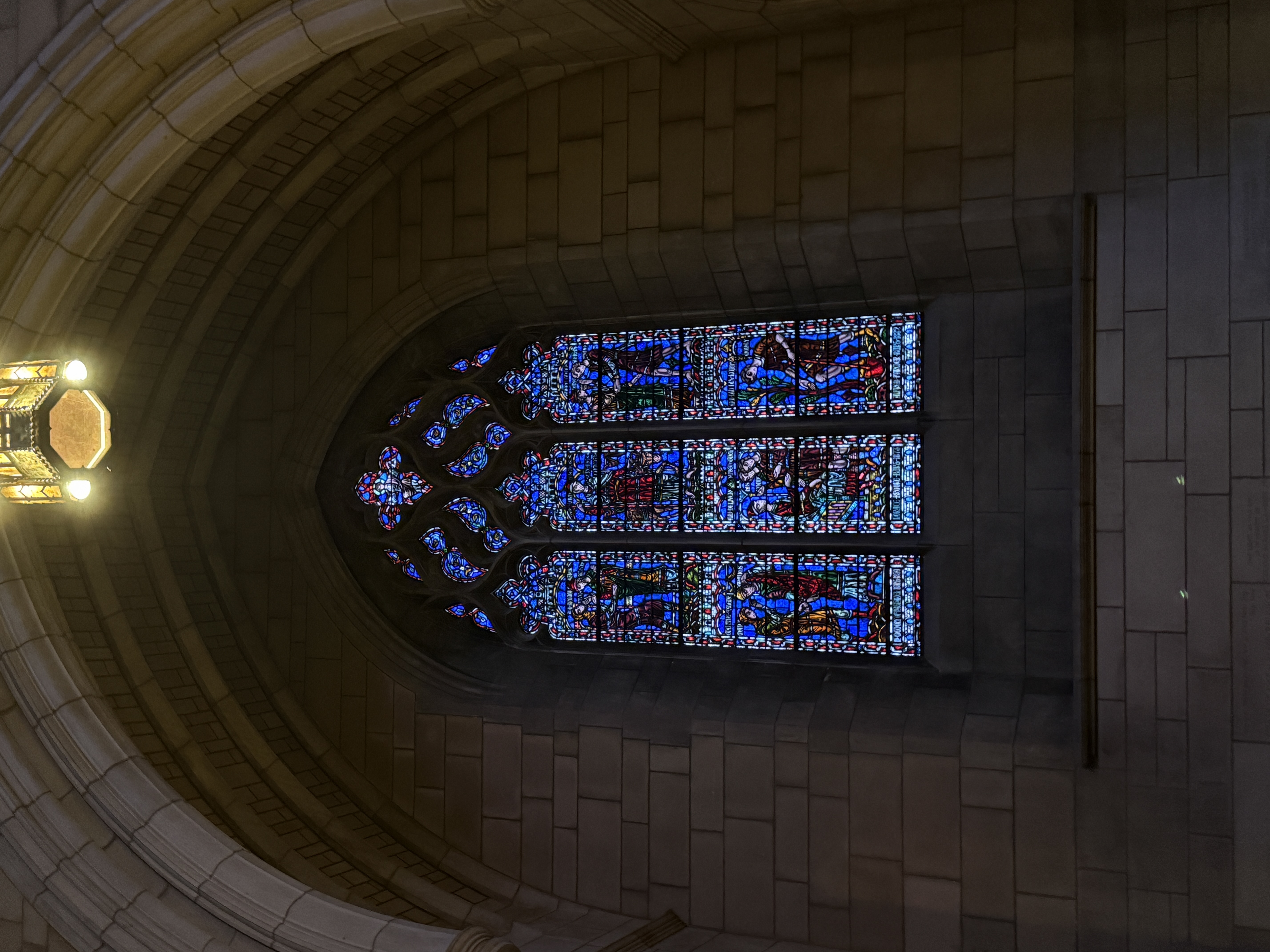 Stained-glass window rising behind a hanging lantern and stone columns