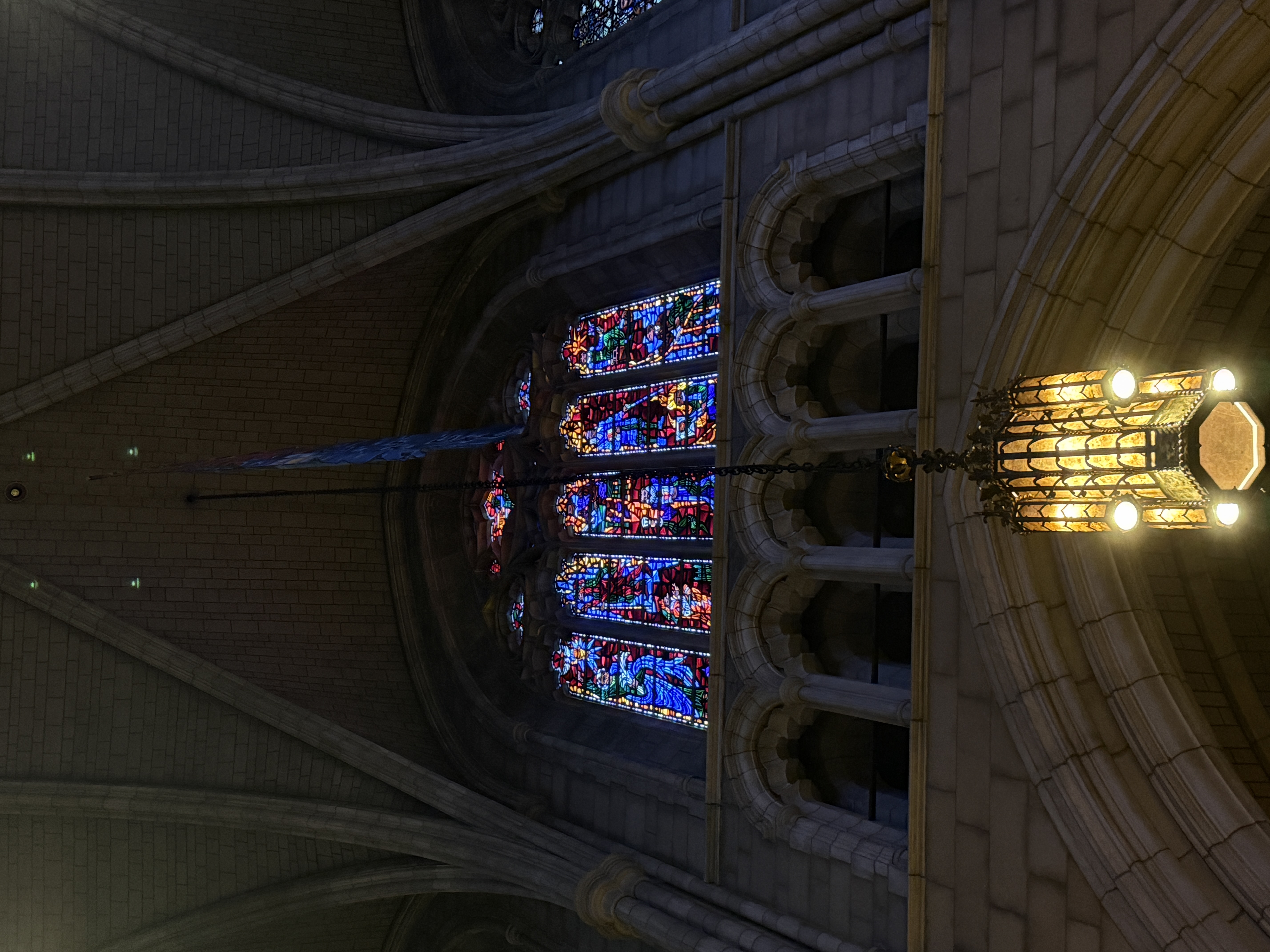 Tall window of stained glass with bright blue scenes and circular tracery