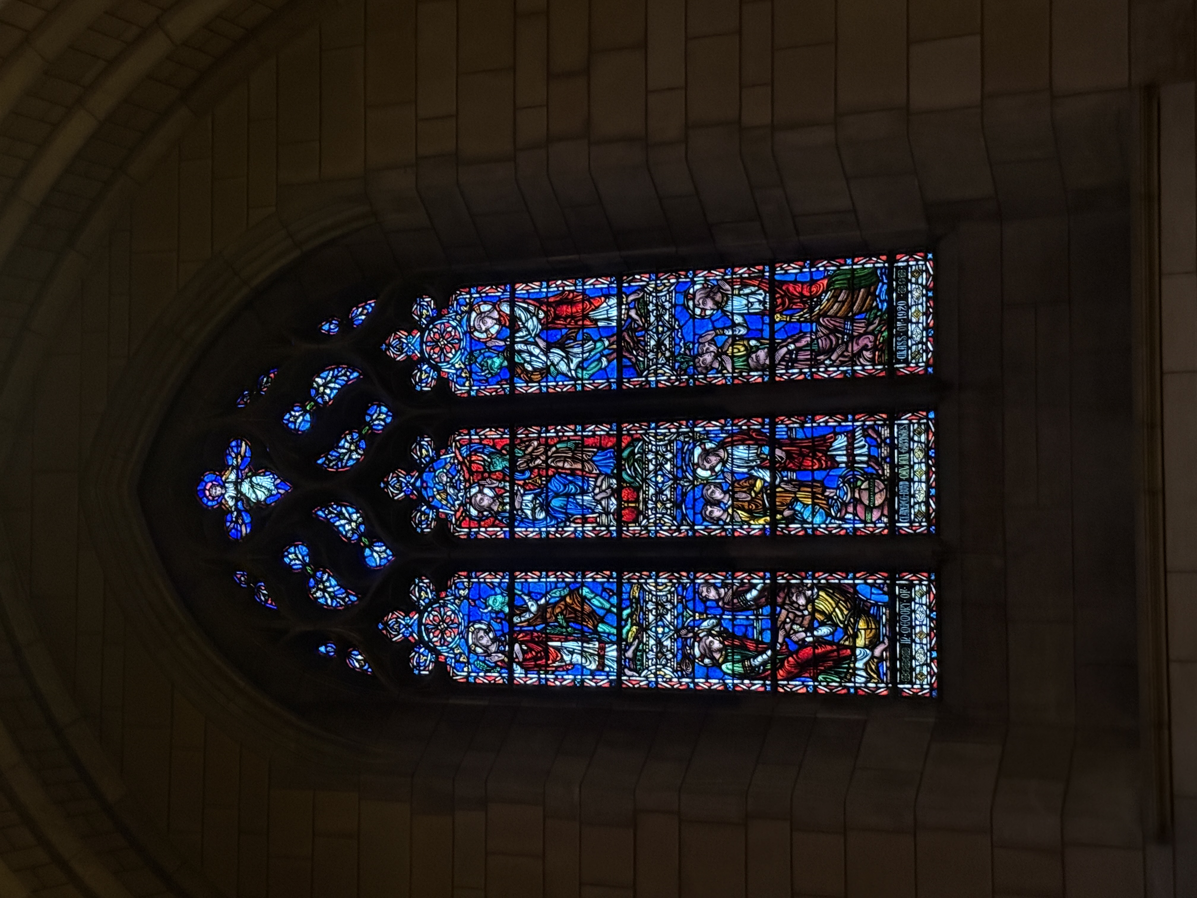 Bright stained-glass lancet window framed by stone ribs and tracery openings