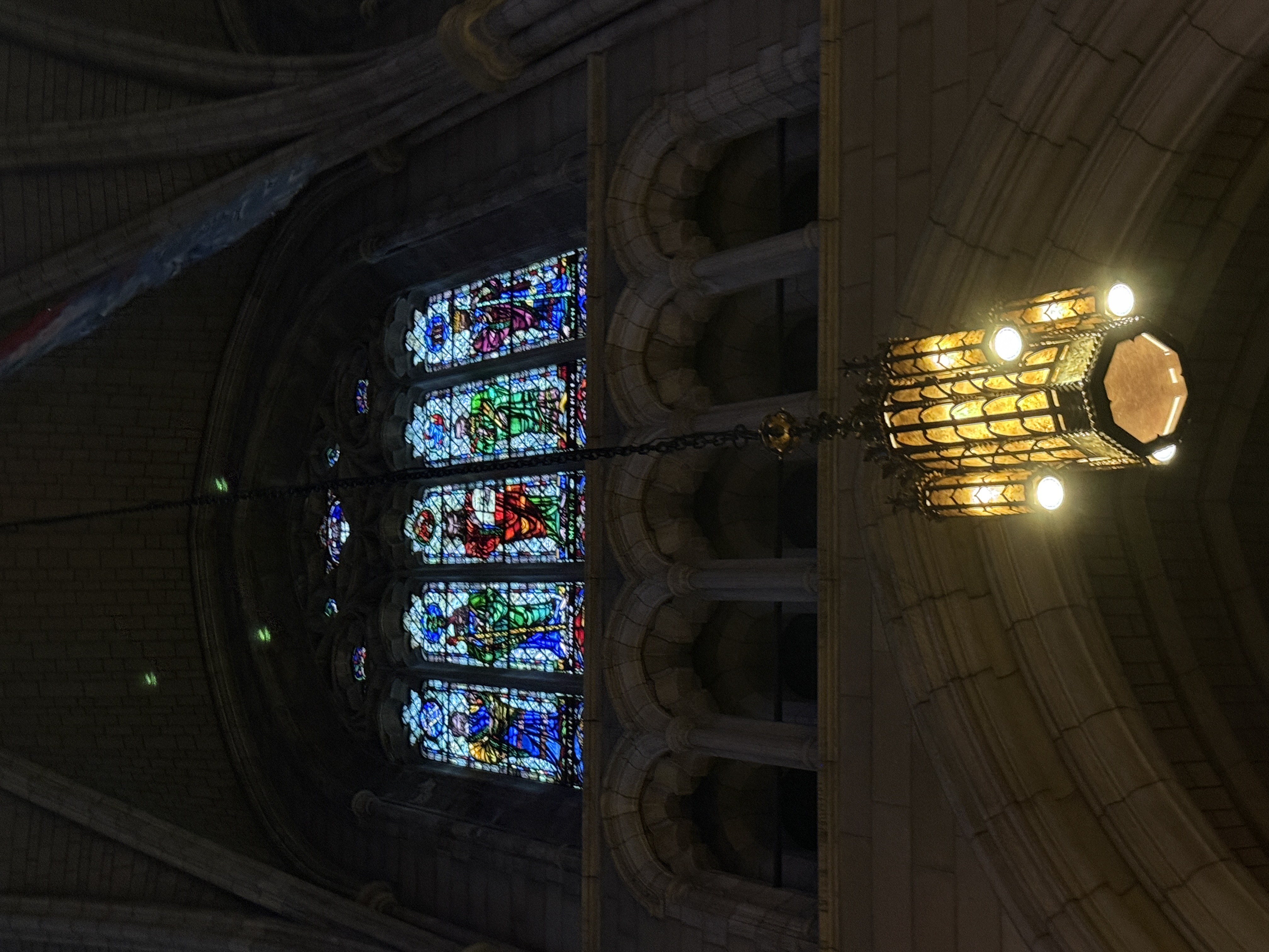 Side chapel view where stained-glass windows rise above dark wooden choir stalls