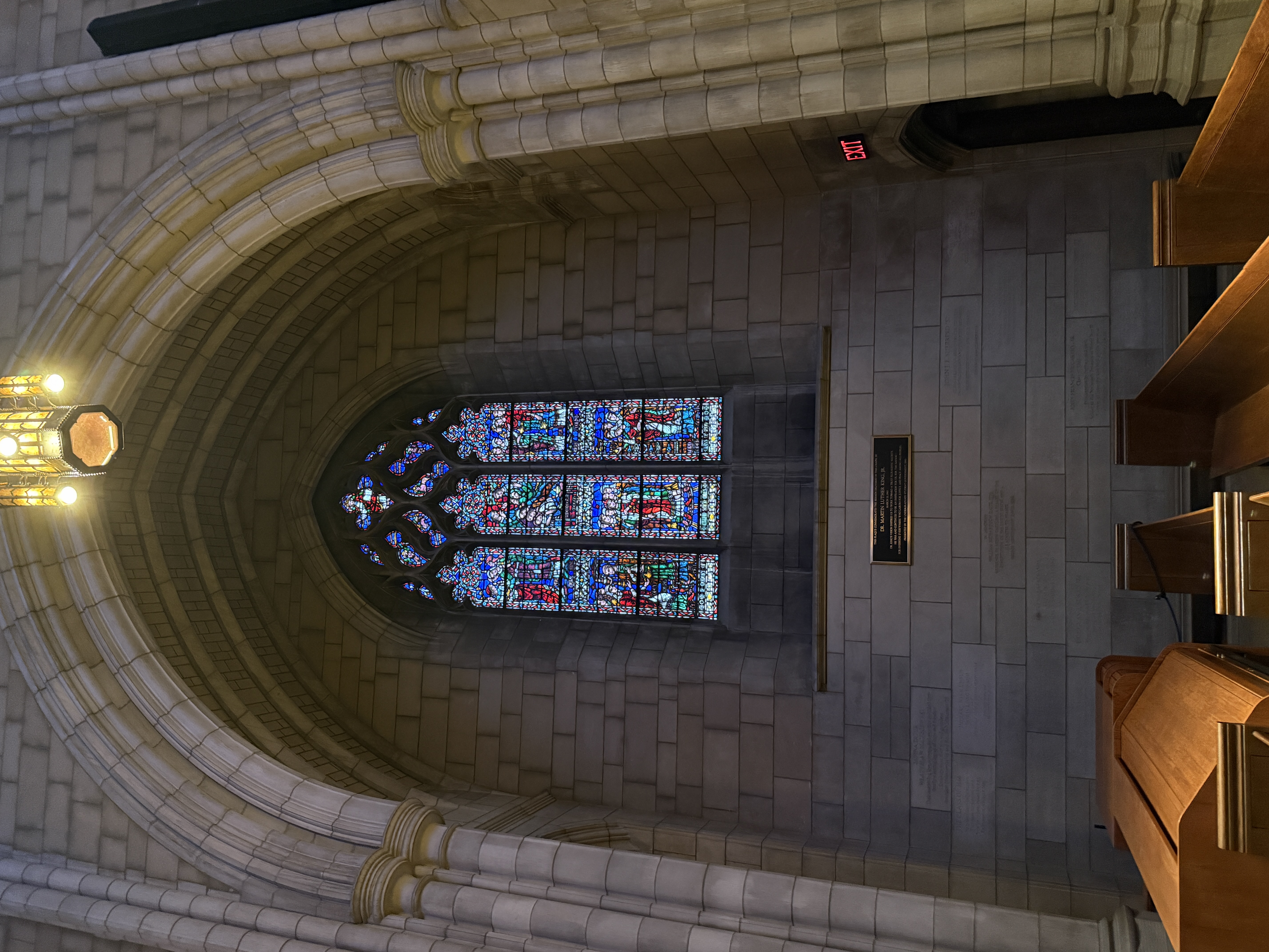 Tall stained-glass window dominated by blue tones and small red figure panels