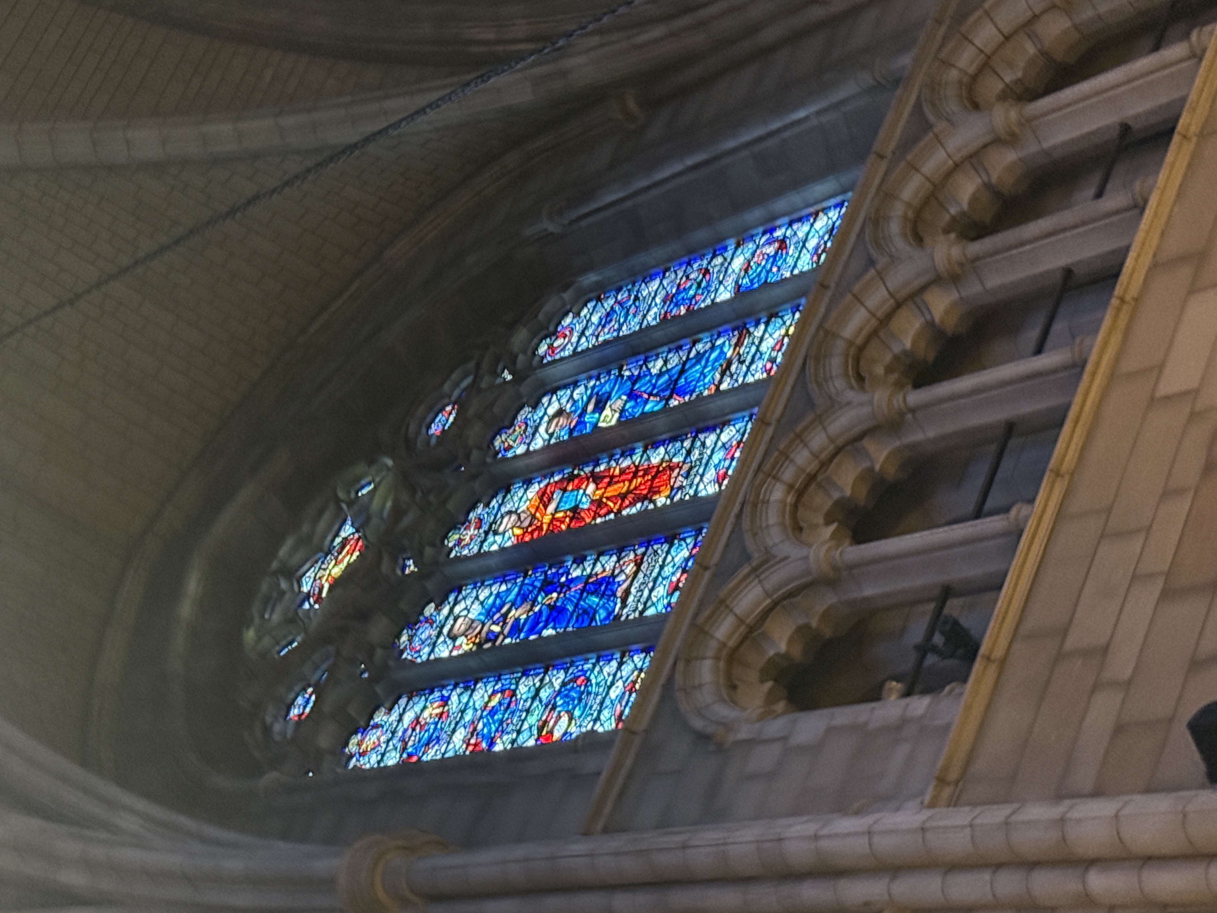 Large stained-glass window glowing above choir seating and stone columns