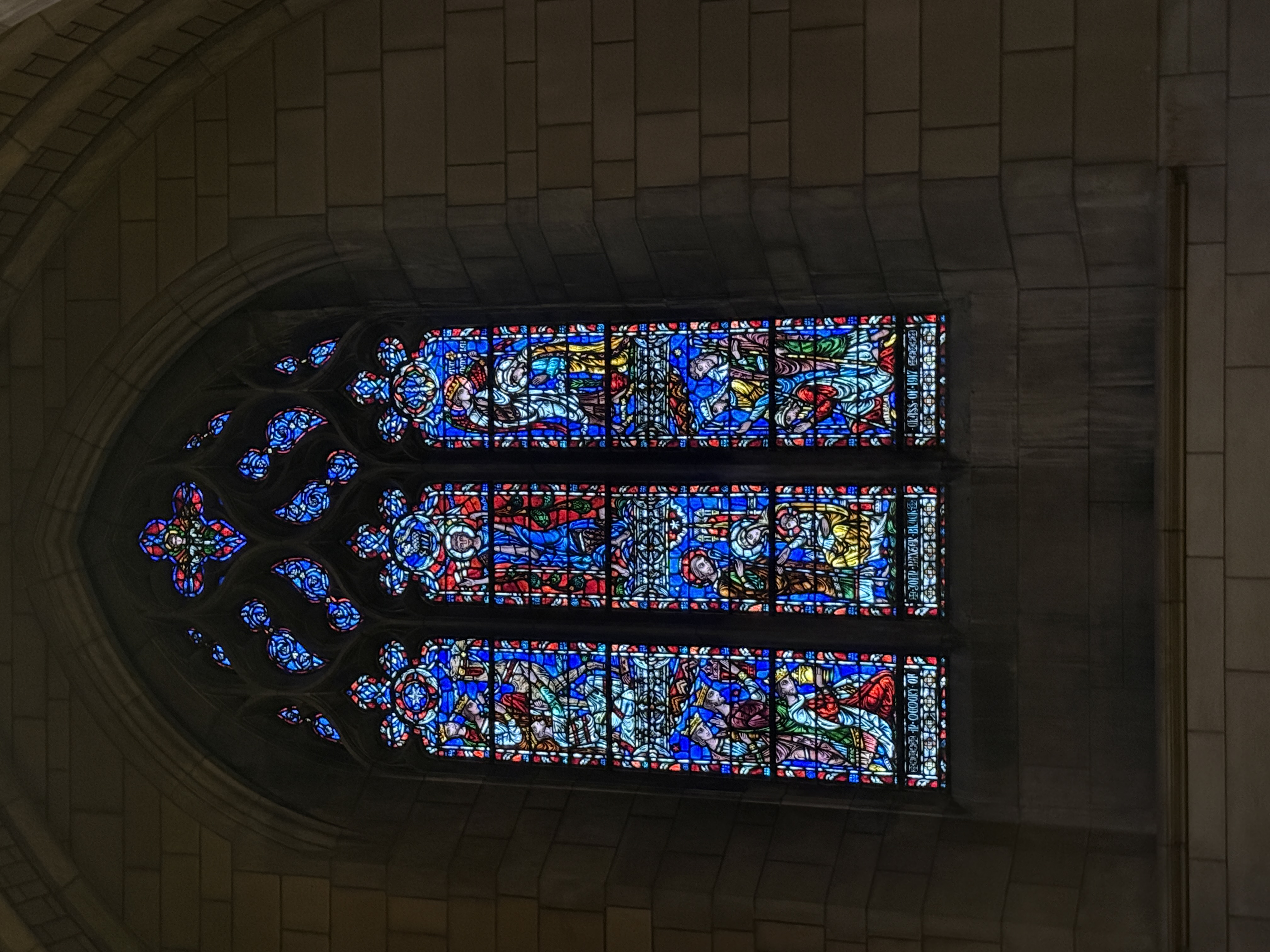 Detailed stained-glass lancet window with three stacked figural panels