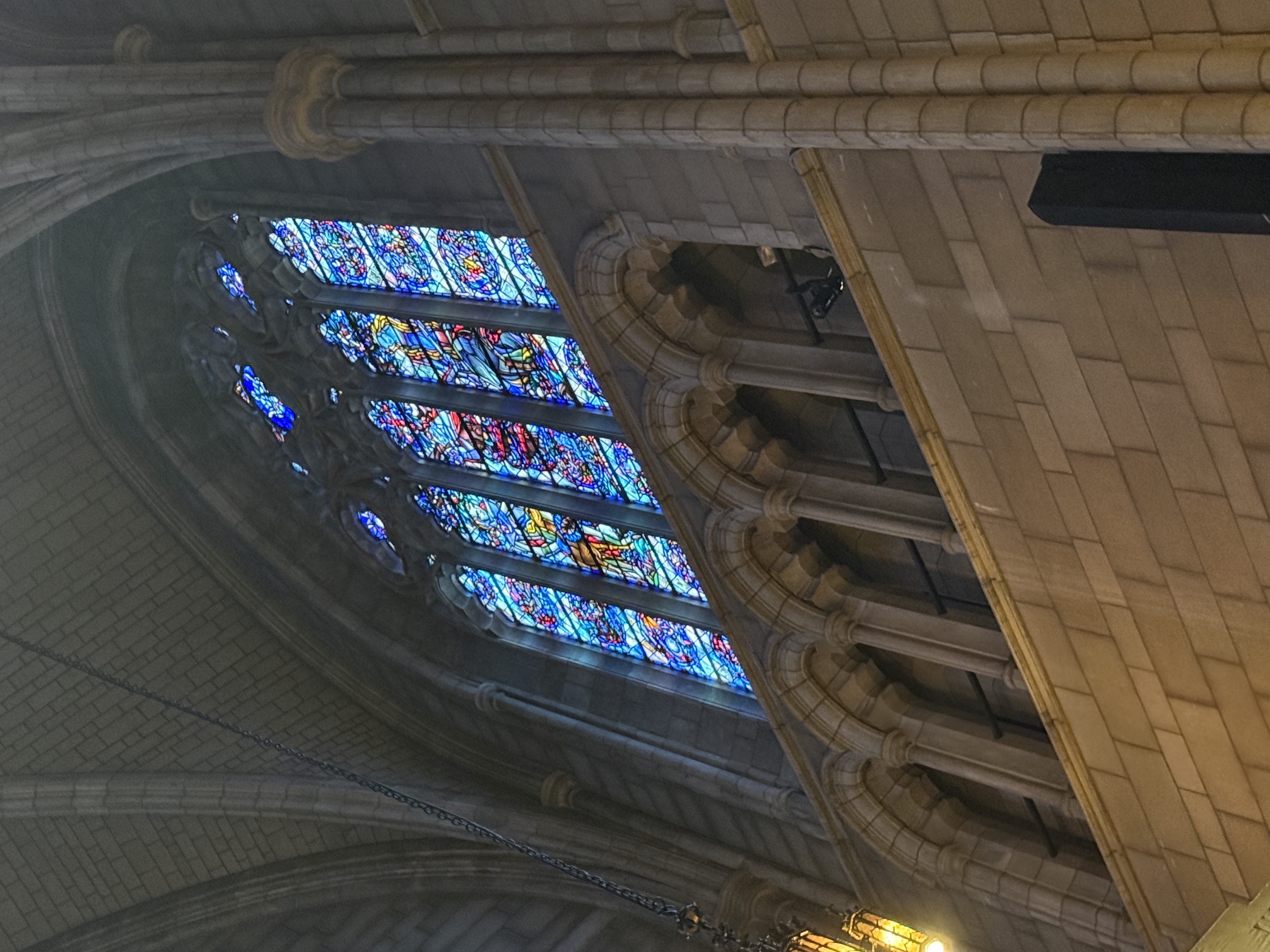 Tall chapel stained-glass window viewed from below with a glowing lantern nearby