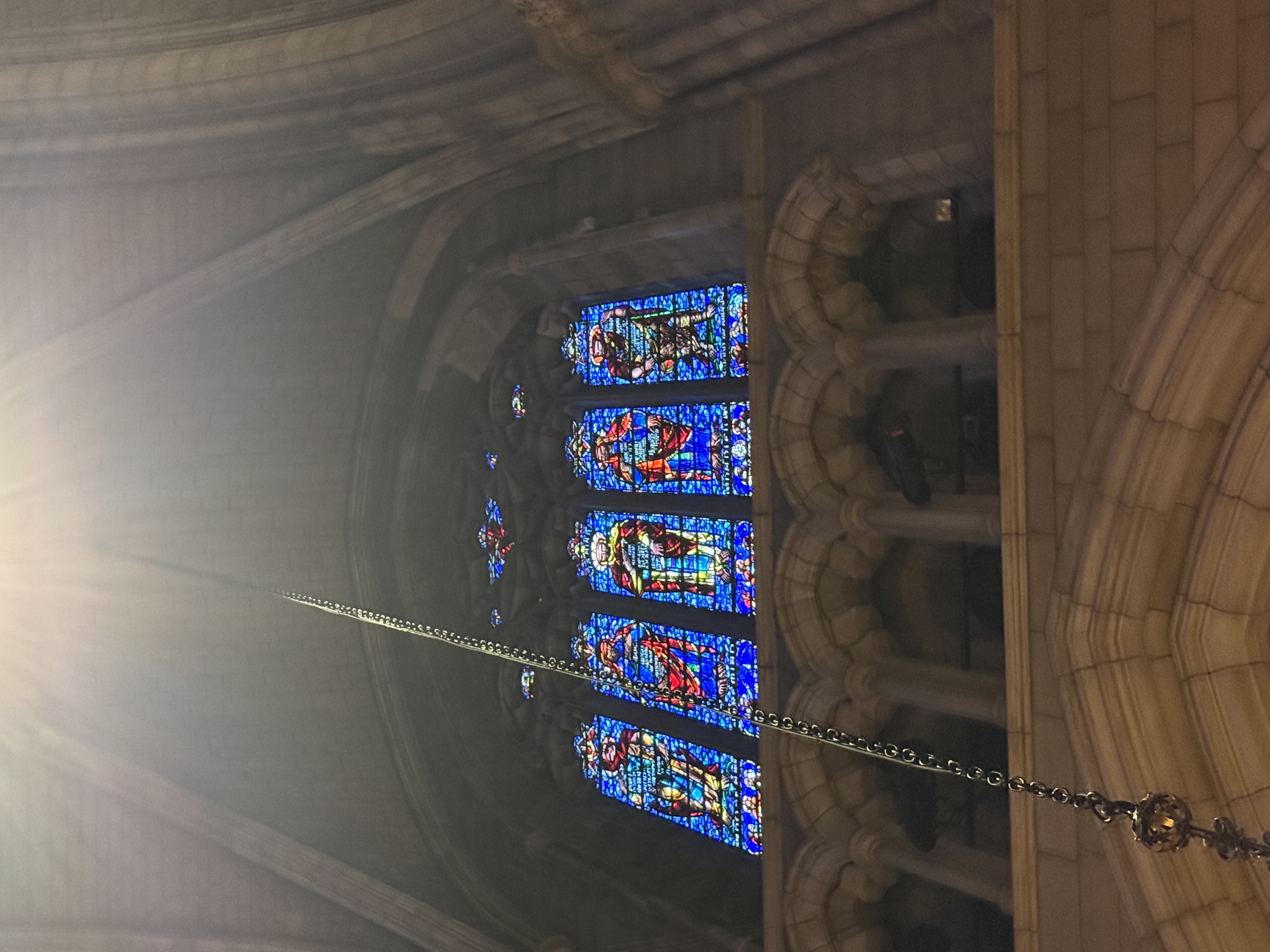 Tall apse window with stained-glass figures viewed through hanging chains