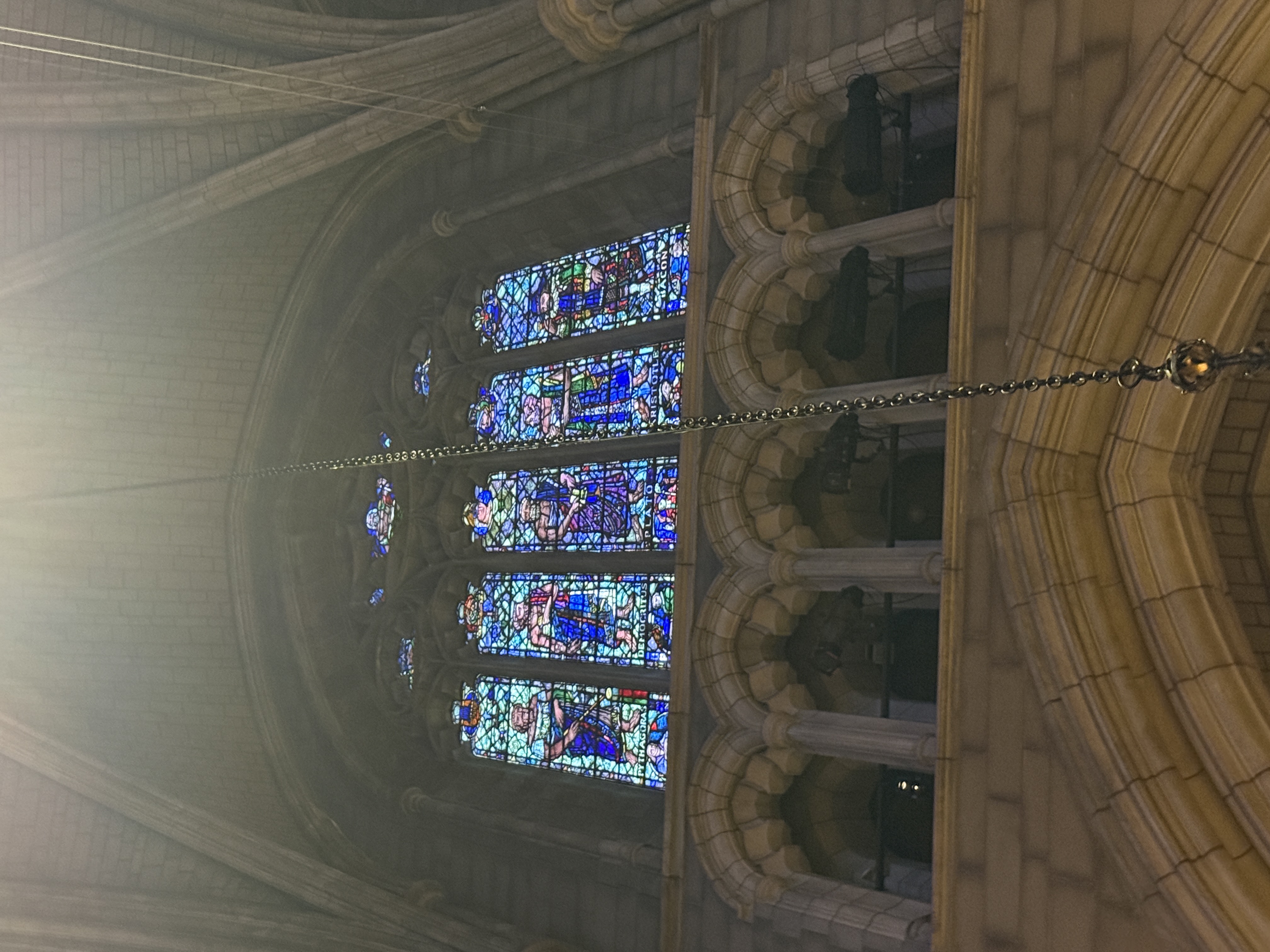 Large stained-glass window of robed figures beneath stone Gothic arches