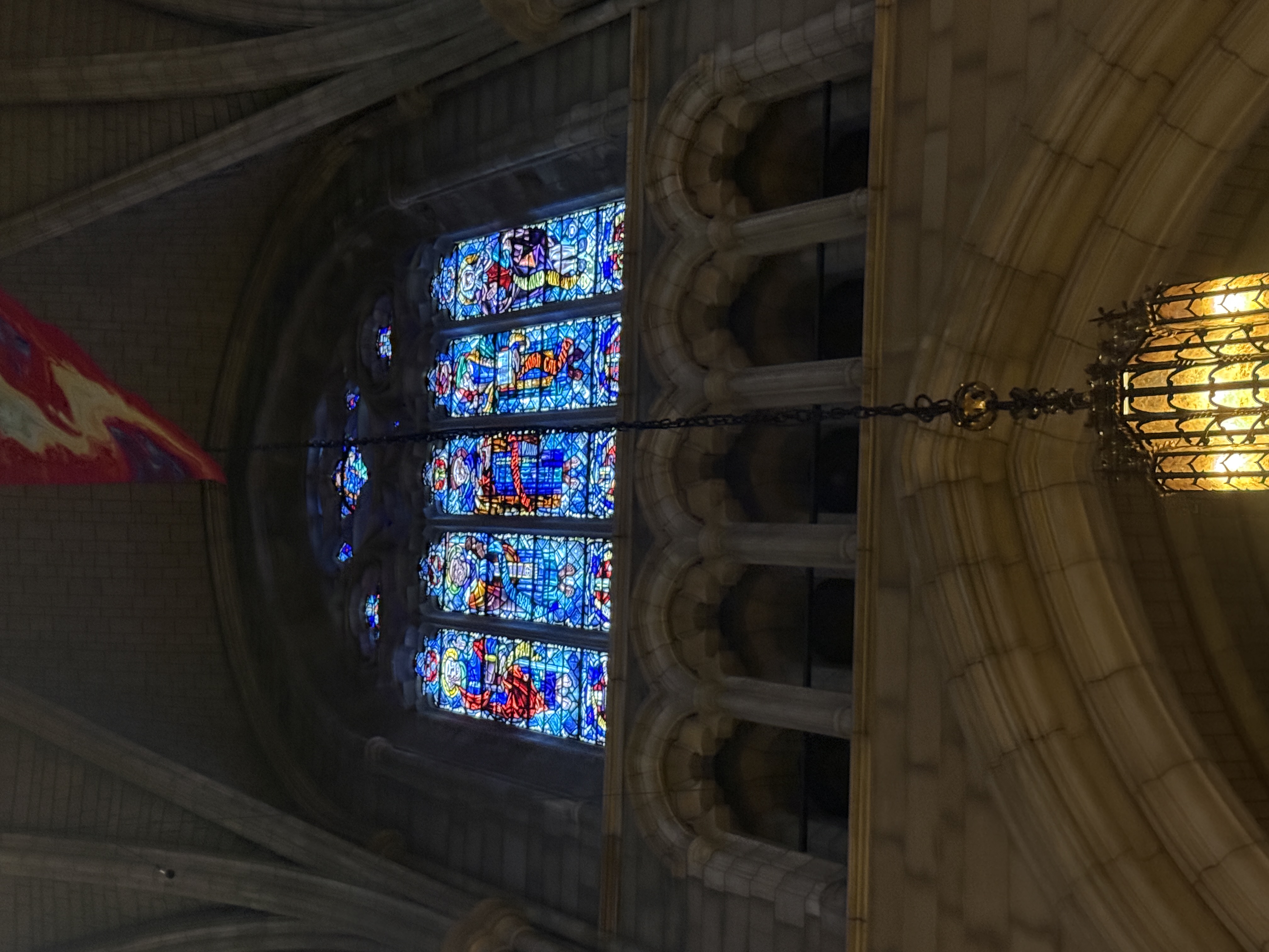 Figural stained-glass window partly framed by a lantern and a hanging banner